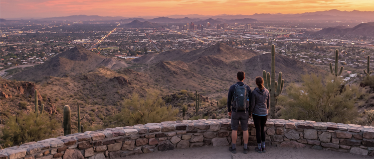 Hikers on a rocky desert trail with saguaro cacti and the McDowell Mountains at sunrise