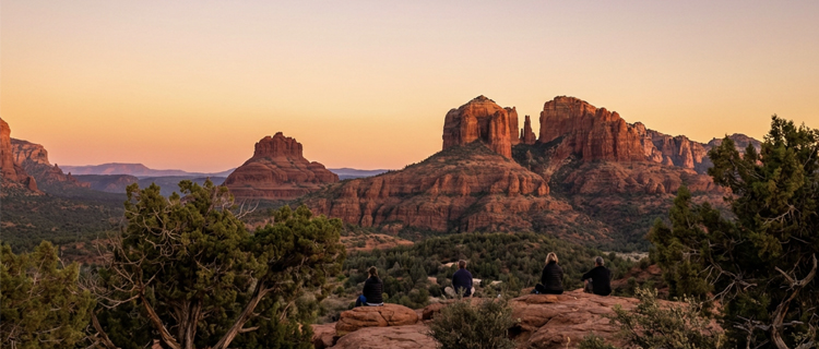 Quiet morning light on a red-rock saddle where a Sedona visitor sits looking out over the canyon