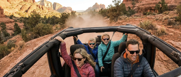 Family with two kids laughing with arms raised in an open-top jeep on a bumpy red-rock trail during a Sedona jeep tour