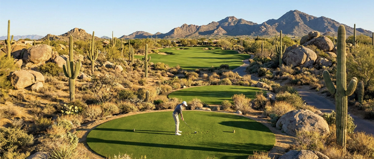 Golfer teeing off on a desert golf hole in Scottsdale, Arizona framed by saguaro cactus, boulders, and mountains